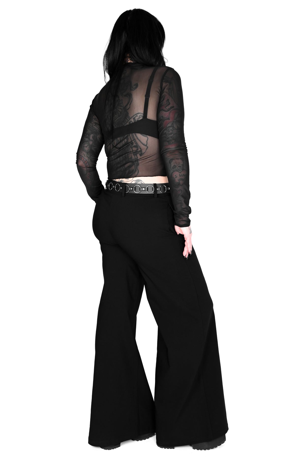 A model shown from the back wearing a sheer black long-sleeve mesh top with a black bralette underneath and wide-leg black pants, set against a plain white background.