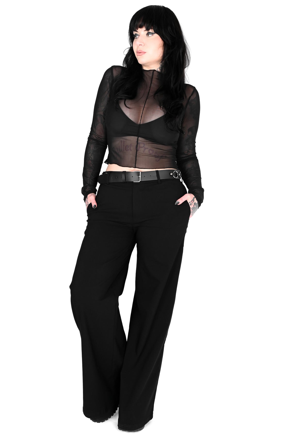 A woman modeling a black sheer long-sleeve mesh top with a black underlayer and black wide-leg pants, standing against a plain white background.