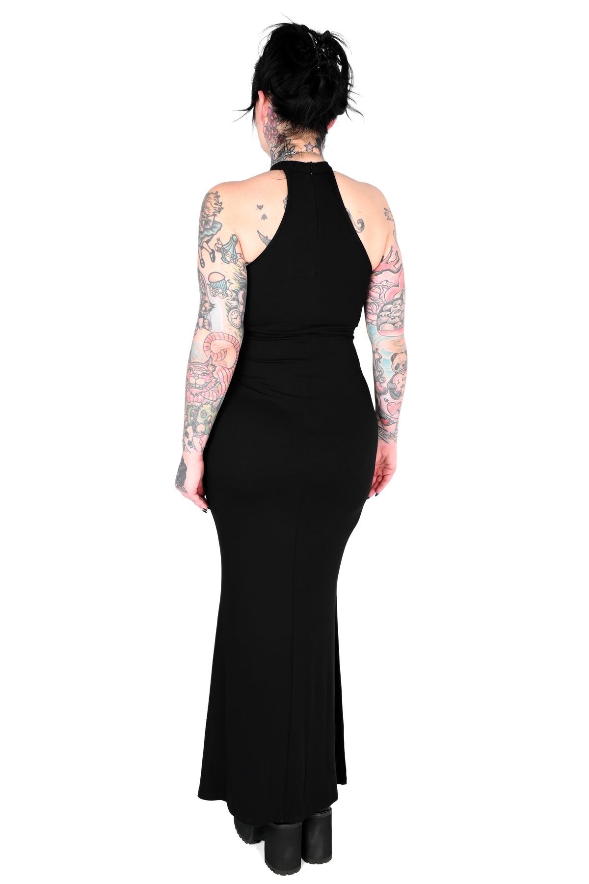 A woman viewed from the back wearing a black halter-neck maxi dress with a fitted silhouette and flared hem, standing against a plain white background.