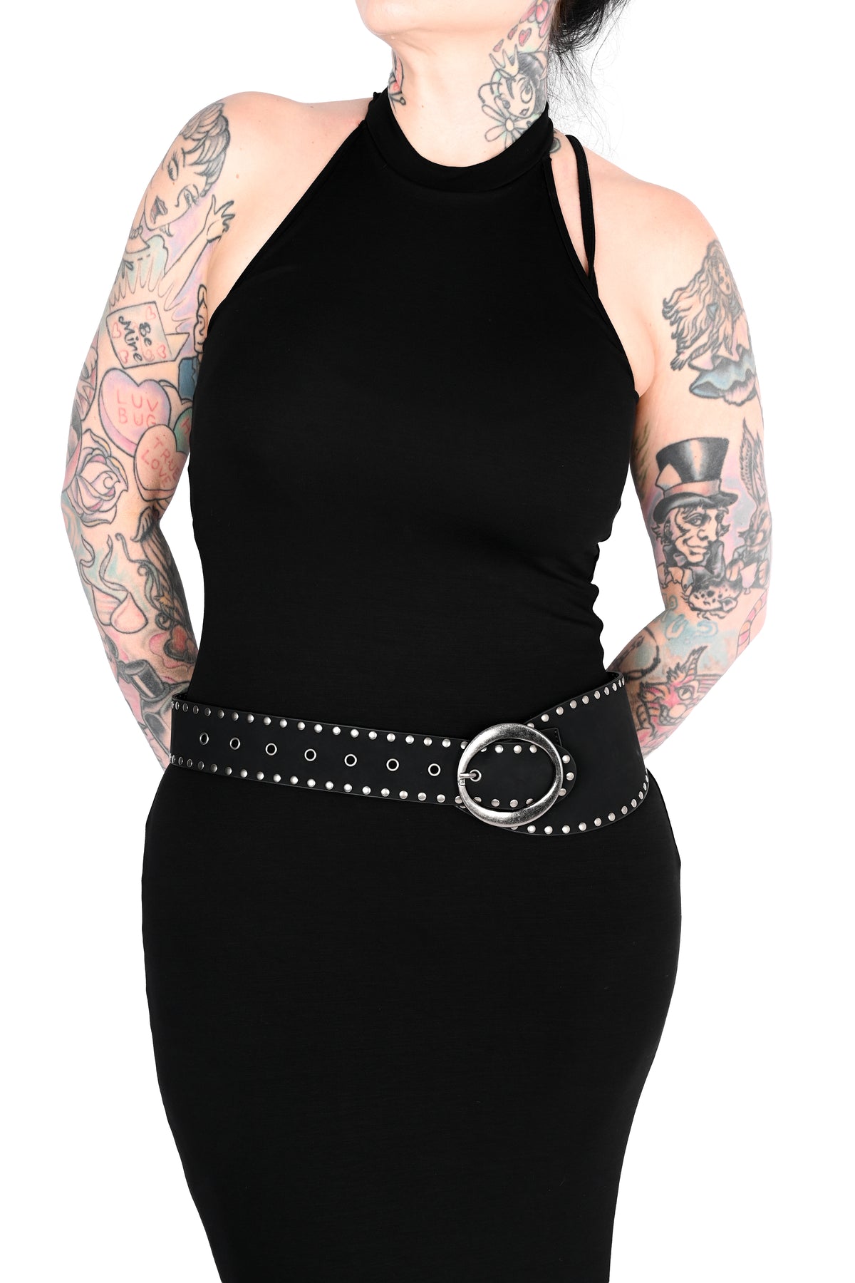 A black halter-neck bodycon dress with a wide black studded belt featuring a silver-tone oval buckle, shown on a model with tattooed arms against a white background.