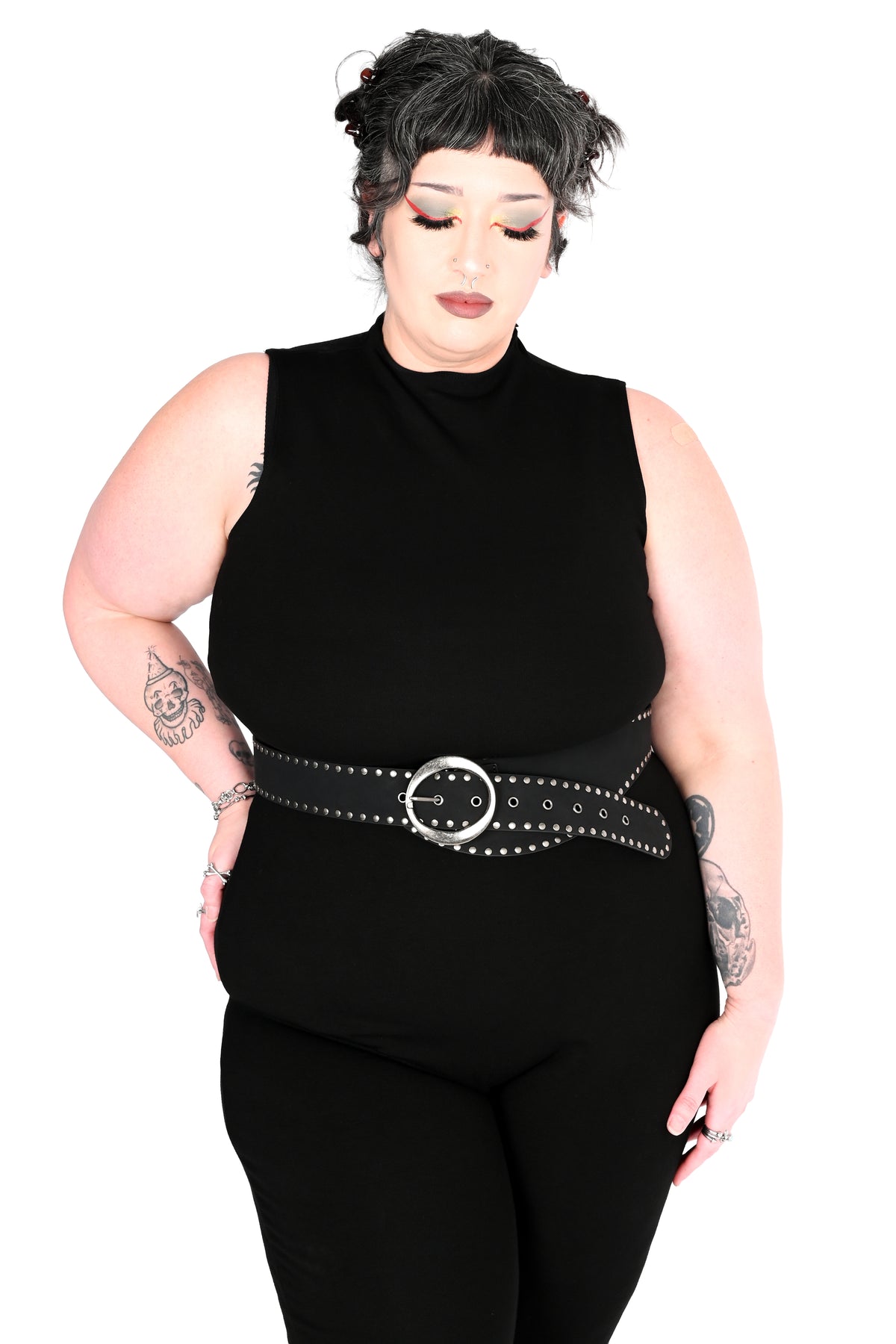 A plus size model in a black halter-neck jumpsuit with a wide black studded belt featuring a silver-tone oval buckle, shown against a white background.