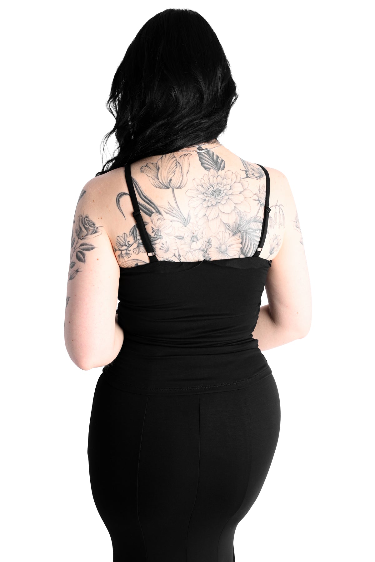 A woman with black hair and floral arm tattoos is shown from the back wearing a black spaghetti-strap top against a plain white background.