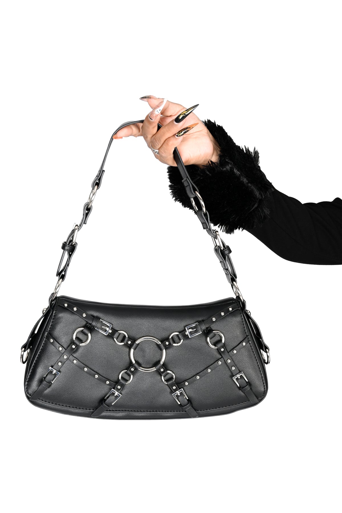 A black faux-leather shoulder bag with silver-tone chain straps, studs, and a central ring detail, held by a hand wearing a black furry sleeve against a plain white background.