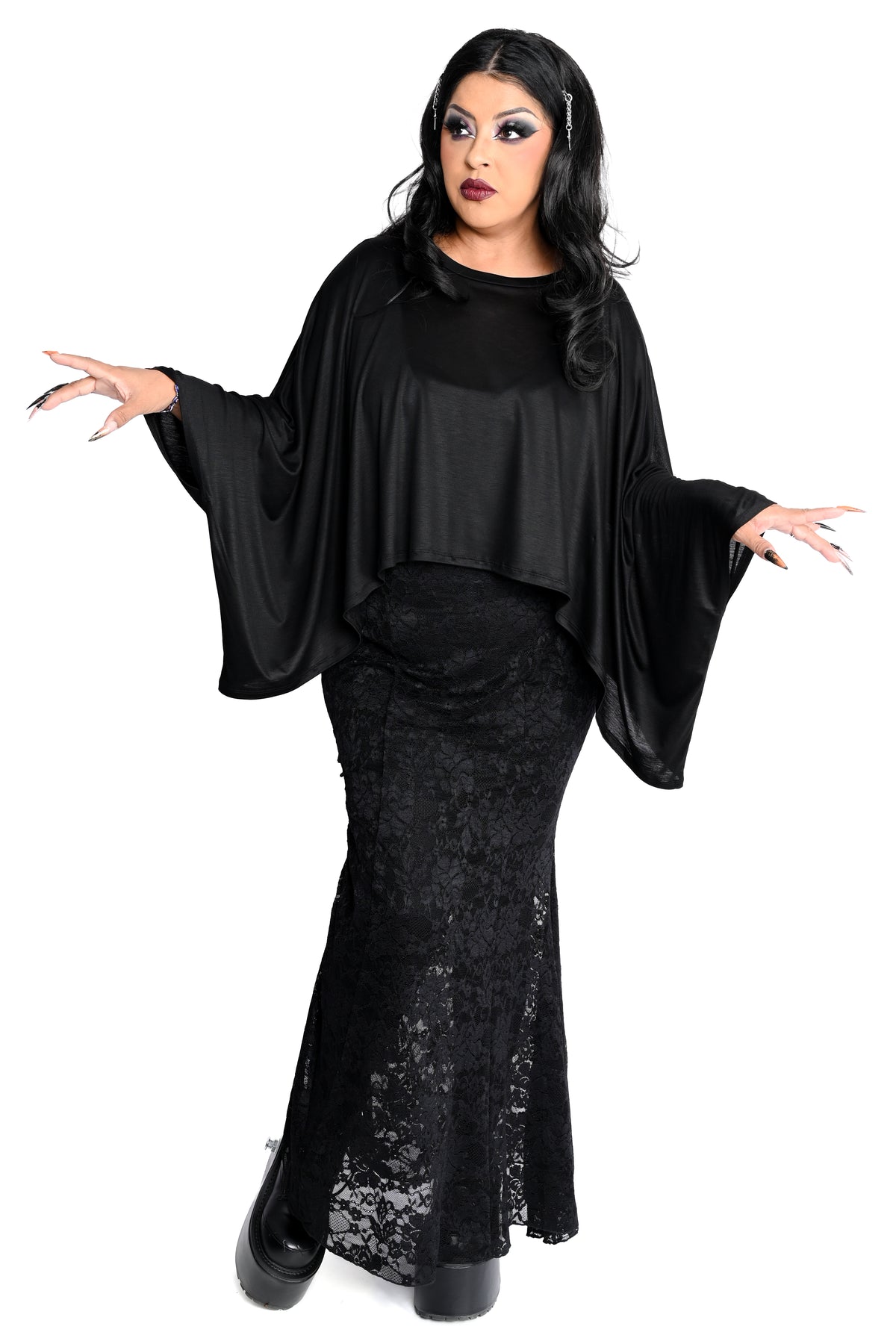 A woman modeling a black gothic-style draped top and a lace mermaid skirt, posed against a solid white background.