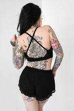 black triangle bralette with lace trim and straps crossed in the back and black shorts with lace trim 